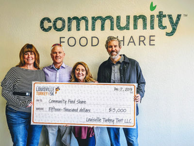 A group of people stand around a large donation check of $15,000 dedicated to Community Food Share from Louisville Turkey Trot LLC.
