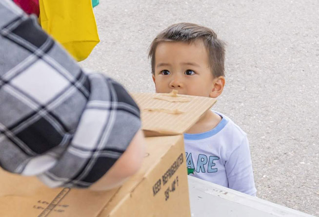 A young boy looks up at an adult opening a cardboard box. 