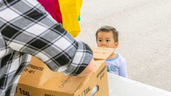 A young child watches as a box is opened at a food distribution.