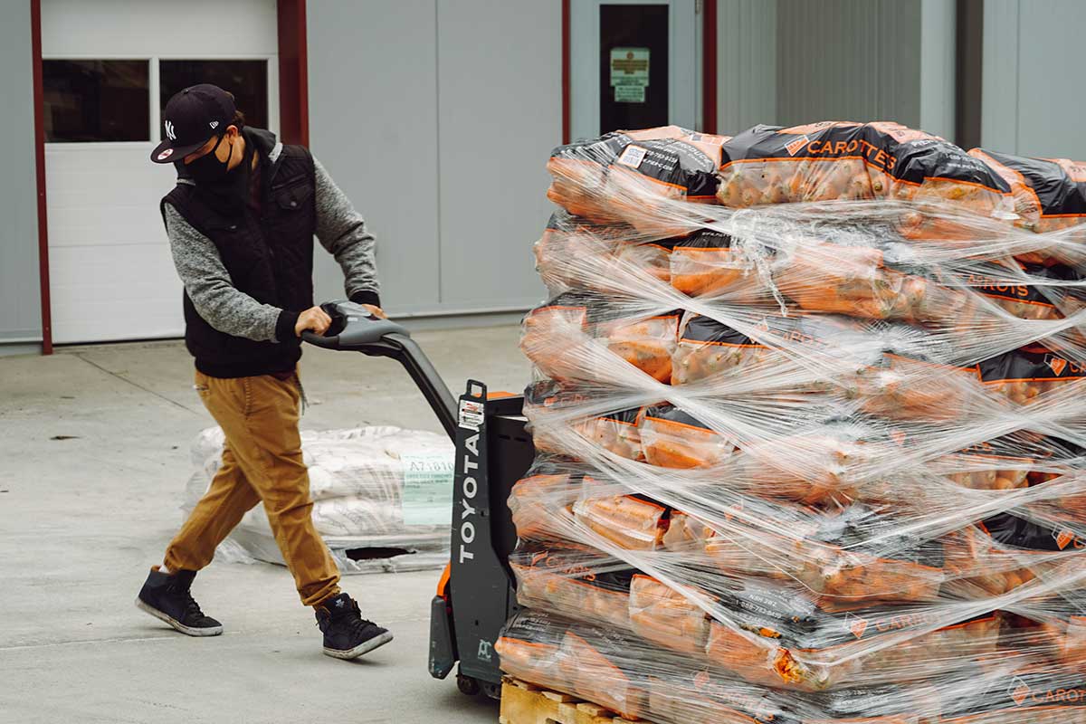 A man navigates a pallet jack full of carrots off of a truck ramp