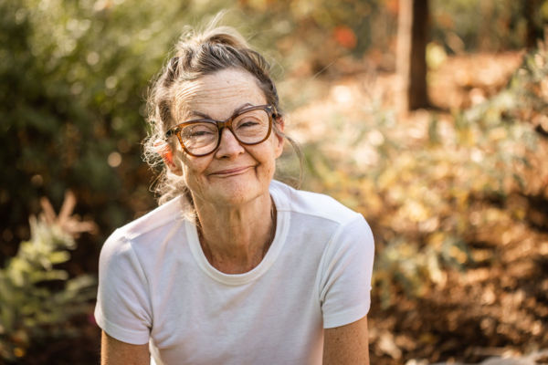 A Woman Wearing Glasses Smiles at Camera Surrounded by Fall Foliage