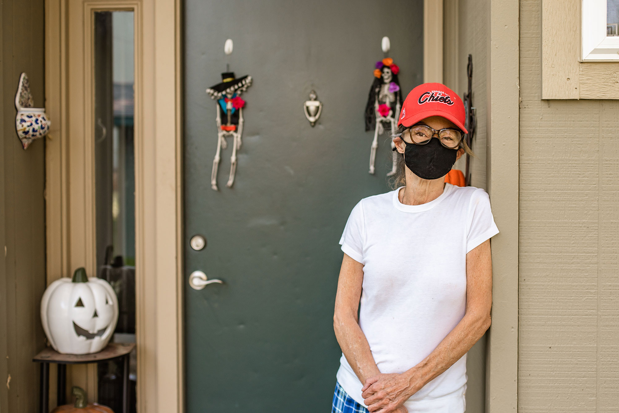 A woman wearing a ball cap leans against her porch