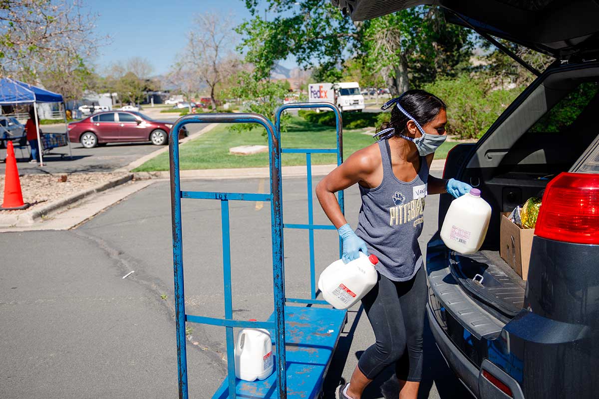 A woman lifts cartons of milk into the trunk of a car