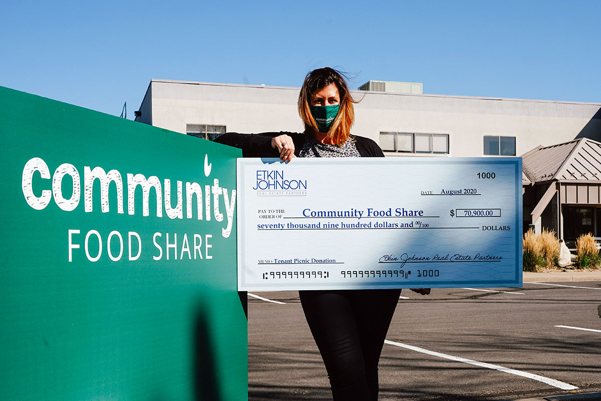 The Executive Director of Community Food Share, Kim Da Silva, holds a large check from Etkin Johnson, symbolic of a gift the company gave the food bank.