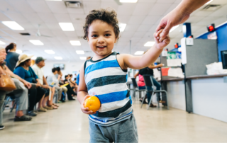 A young boy smiles while holding an orange at a summer meals program