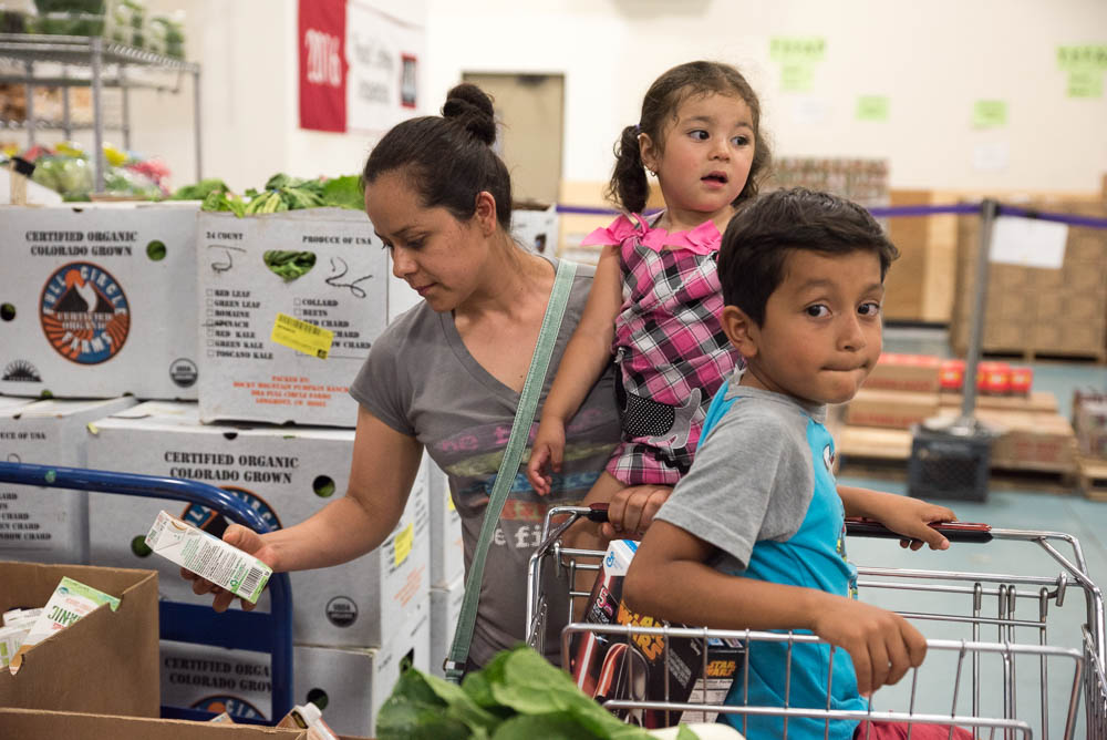 A woman browses groceries while her son and daughter sit in the grocery cart