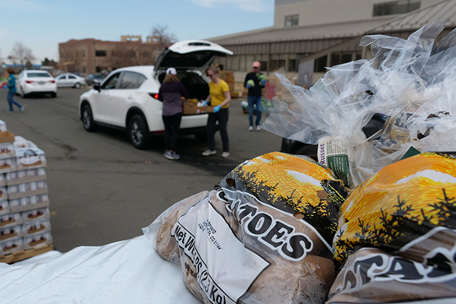 A bag of potatoes sits in the foreground of a drive-through food distribution