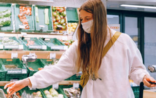 A white woman with long dirty blonde hair reaches for produce in a grocery store